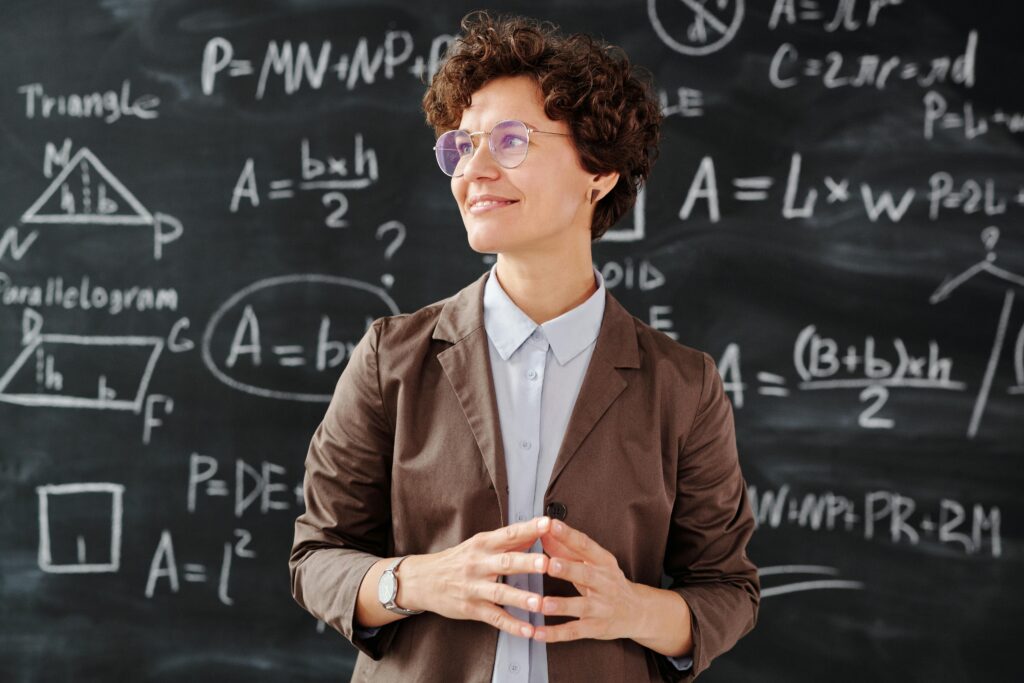 Smiling female teacher standing in front of a mathematical blackboard, illustrating complex equations and teaching concepts.