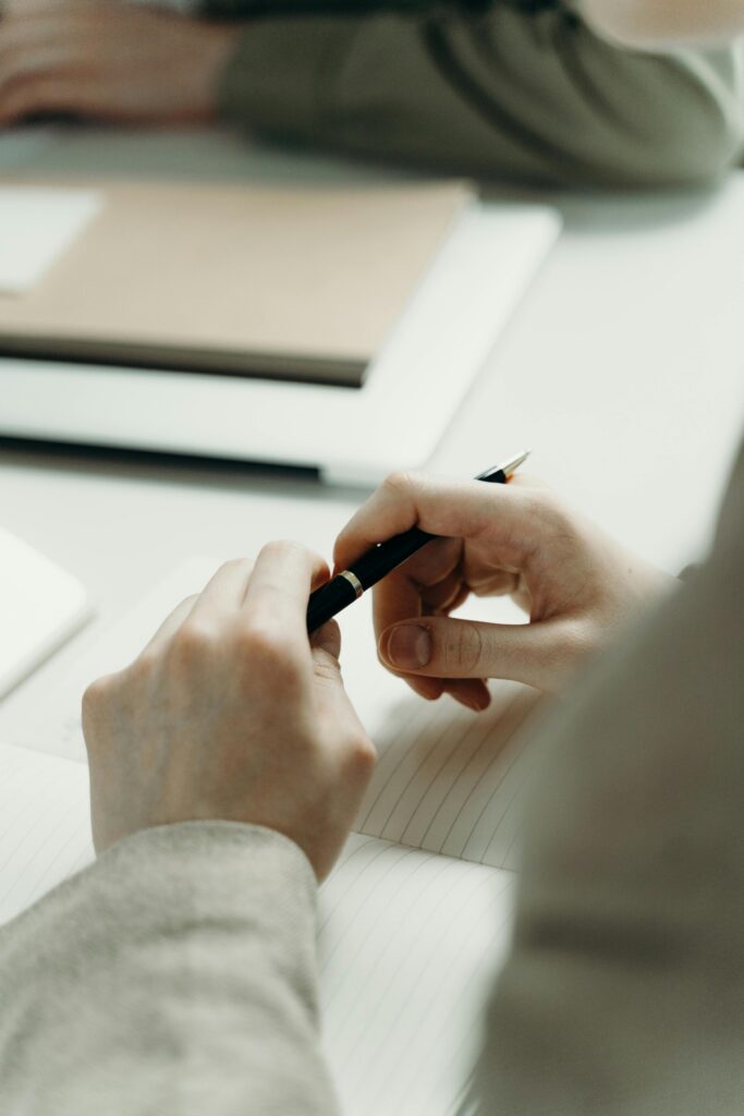 A close-up of hands holding a pen while writing on paper in an office setting.